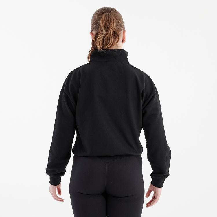 Back view of a woman wearing a black cropped 1/4 zip sweatshirt