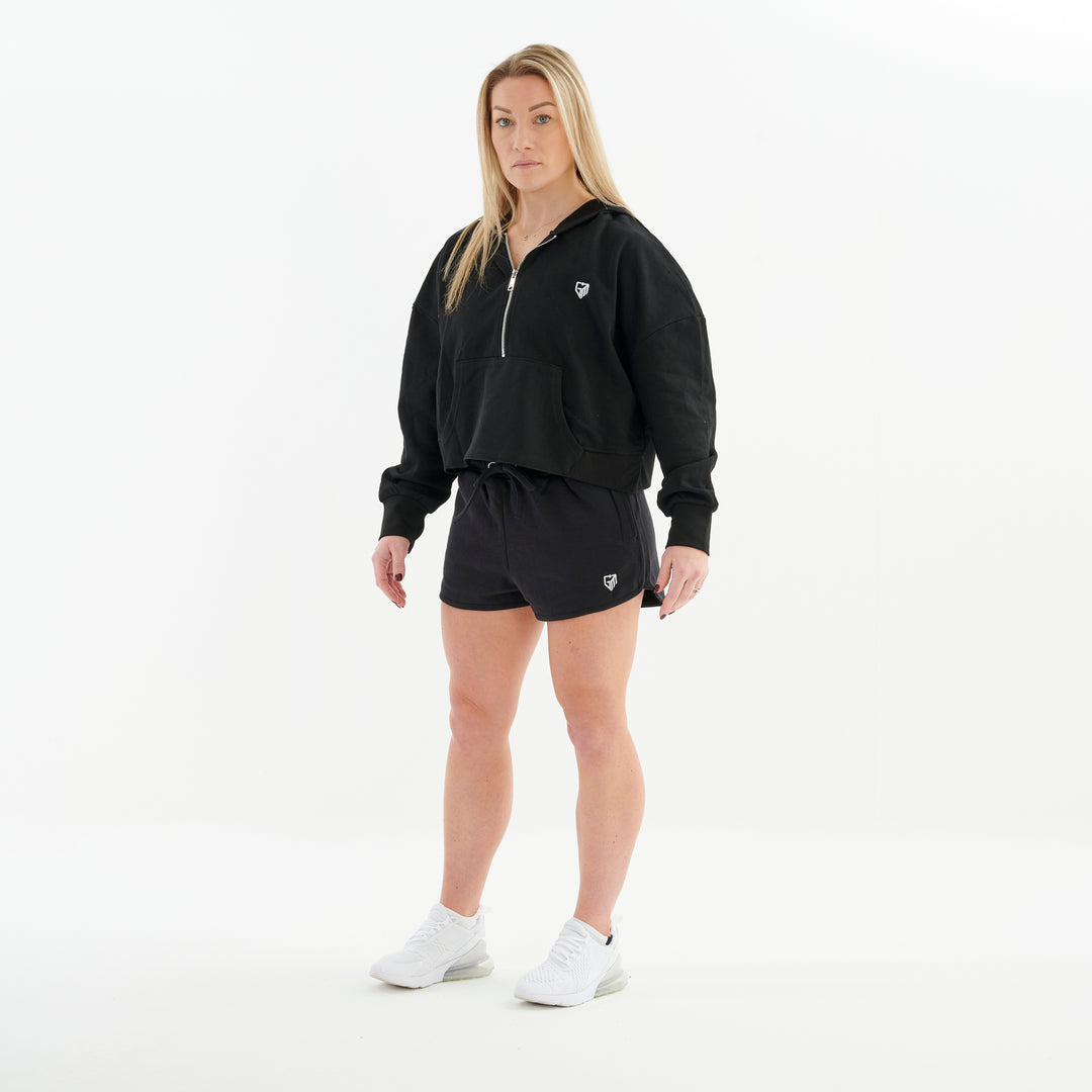 Side view of a woman wearing a half zip cropped hoodie in black