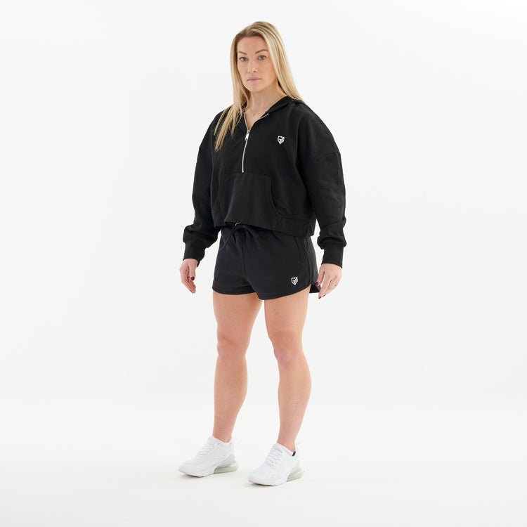 Side view of a woman wearing a half zip cropped hoodie in black